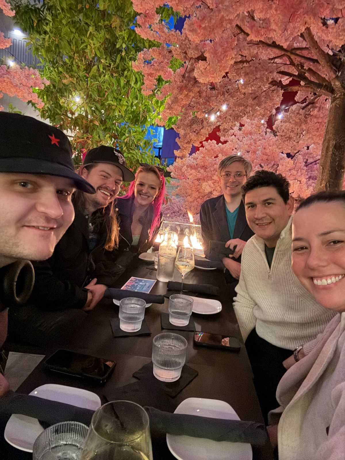 Titus Quarles and five other adults smile for a selfie at a shared restaurant table with pink blooms and green leaves in the background.