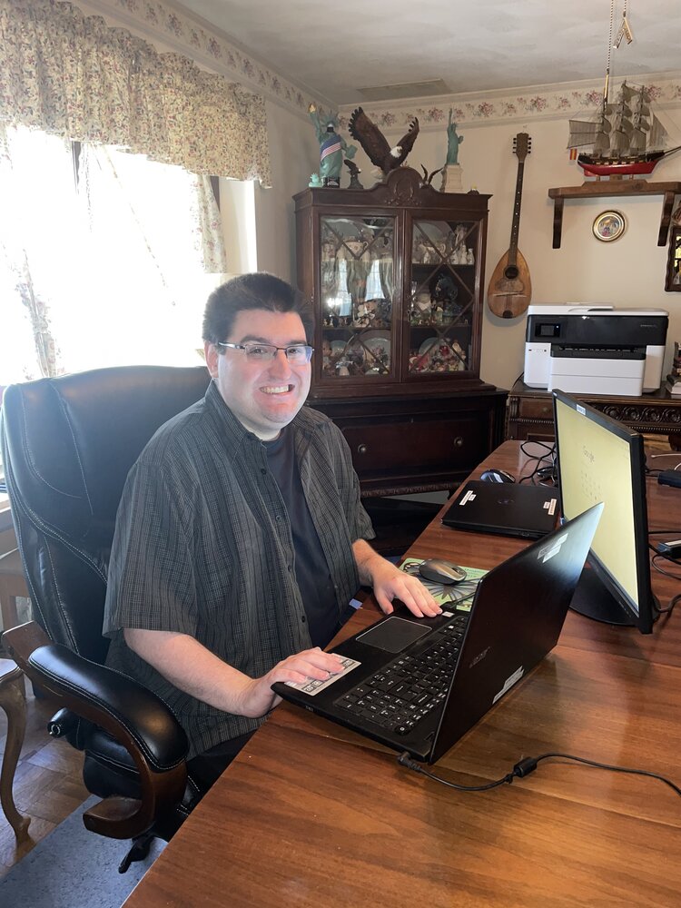 Alex Dudasik works on a laptop at a wood table in his home.