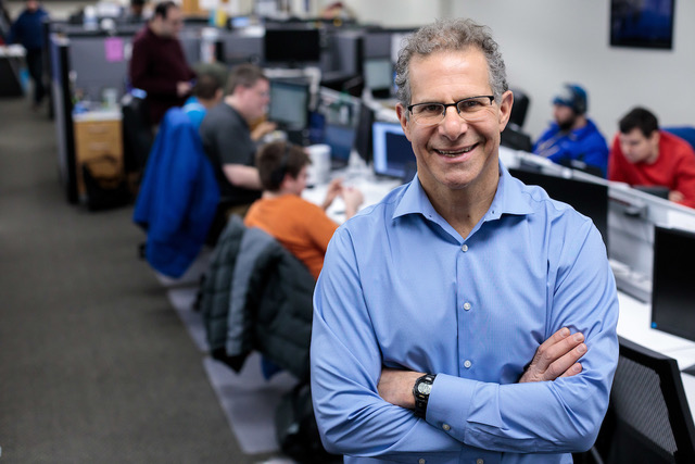 Brad Cohen stands smiling in front of a long desk with his arms crossed.