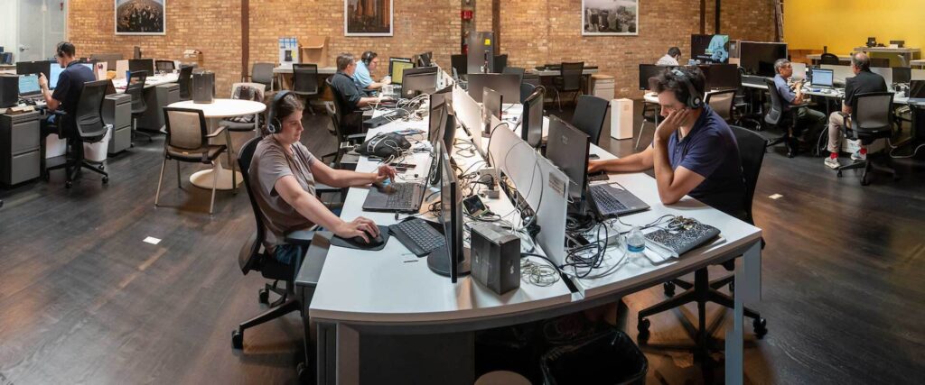 Adult male and female employees work at computers on both sides of a large desk.