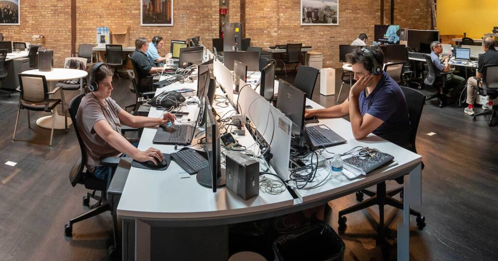 Adult male and female employees work at computers on both sides of a large desk.