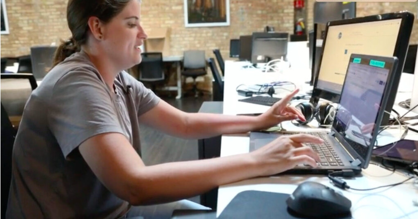 An adult female performs accessibility testing with multiple devices using assistive technologies and a laptop computer.