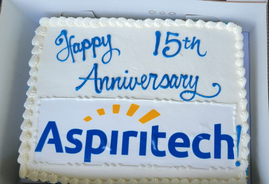 A white frosting cake with the message "Happy 15th Anniversary Aspiritech!"