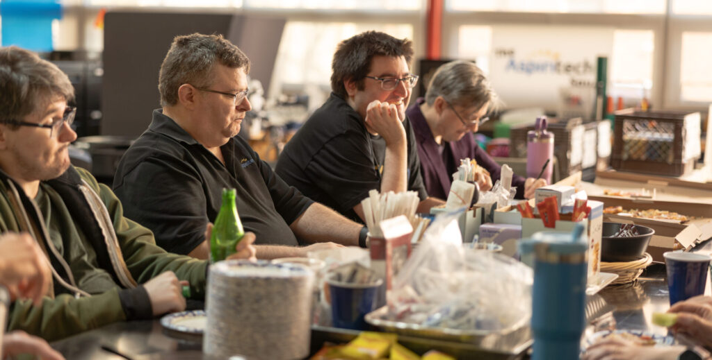 A group of several Aspiritech employees sit and talk around a lunch table.