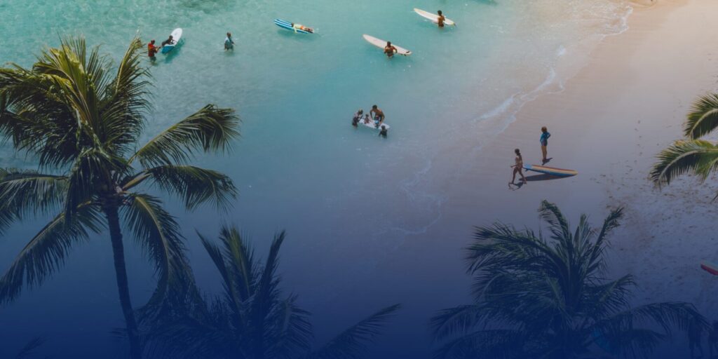 A view of an ocean beach with palm trees and surfers.