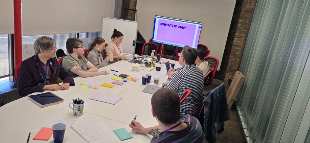 Members of Aspiritech's Creative Services team take notes around a large table in a conference room, looking toward a purple screen that reads, "Empathy Map."