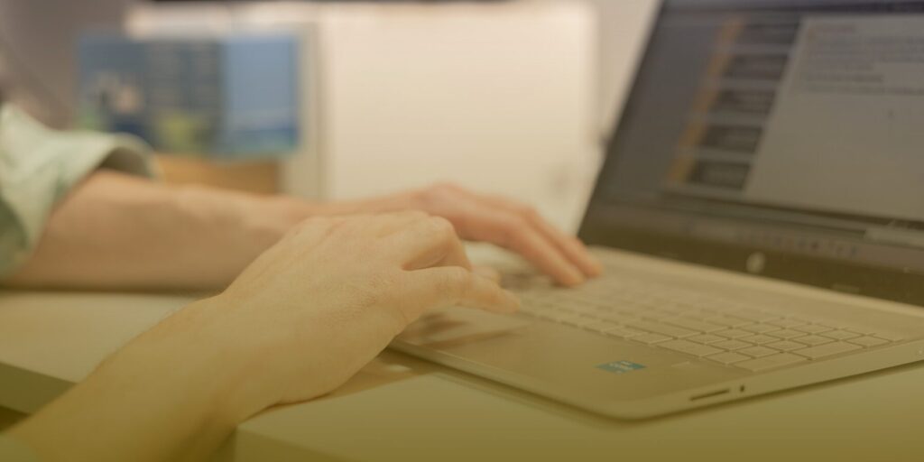 Hands type at a gray laptop keyboard, with a gradient yellow graphic overlay.