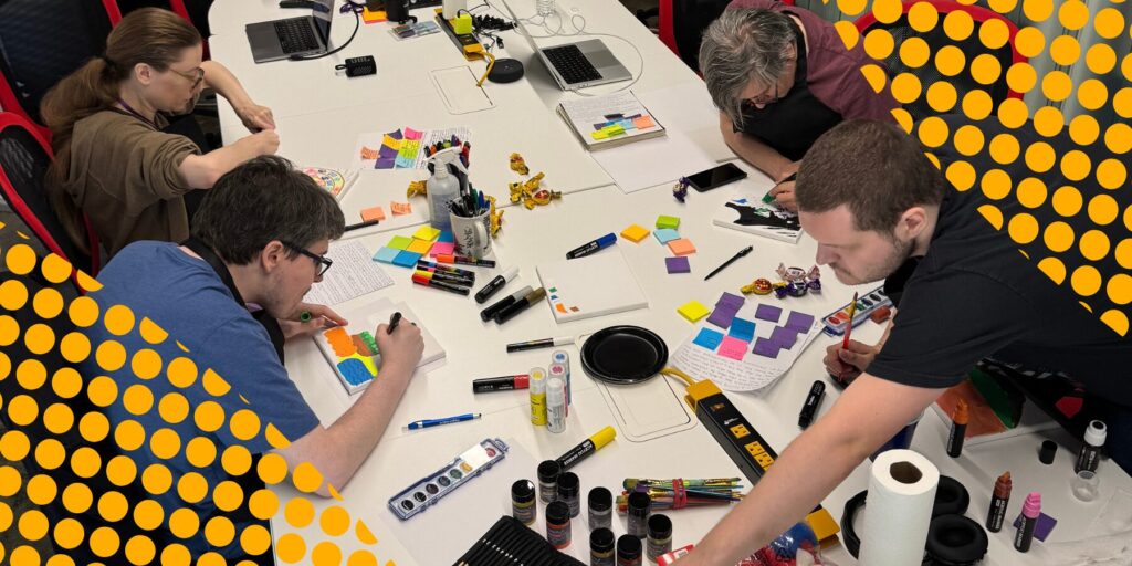 An overhead shot of four Aspiritech team members working with various art supplies on a long white table.