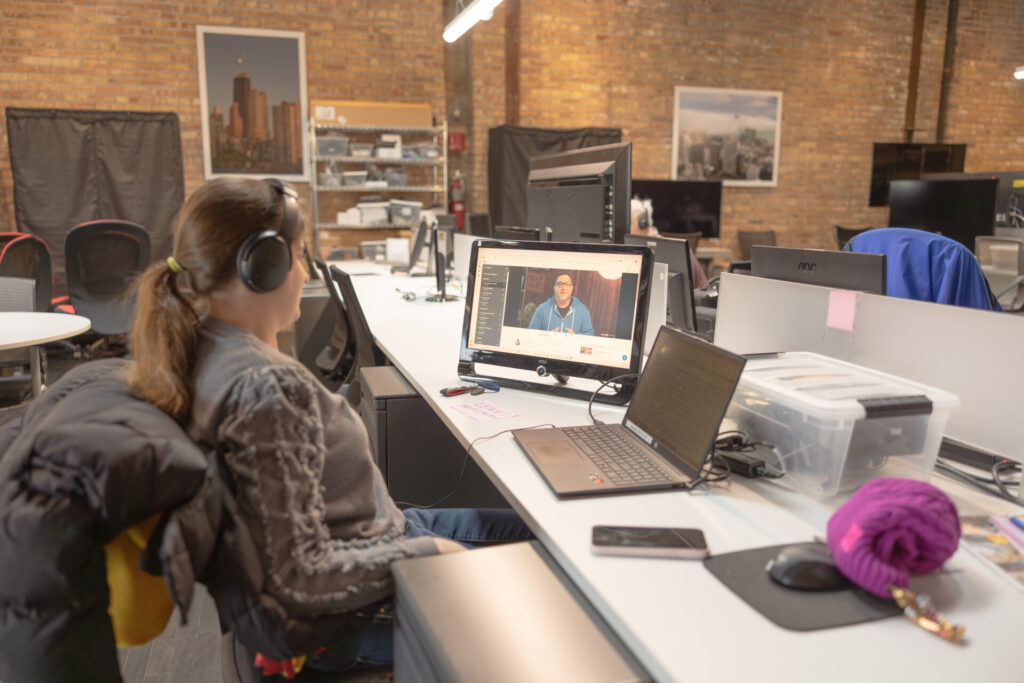 A female Aspiritech employee wears headphones while watching a video on a computer screen.