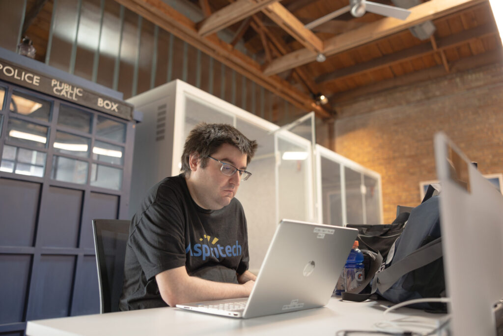 A male Aspiritech employee works at a laptop on a white desk.