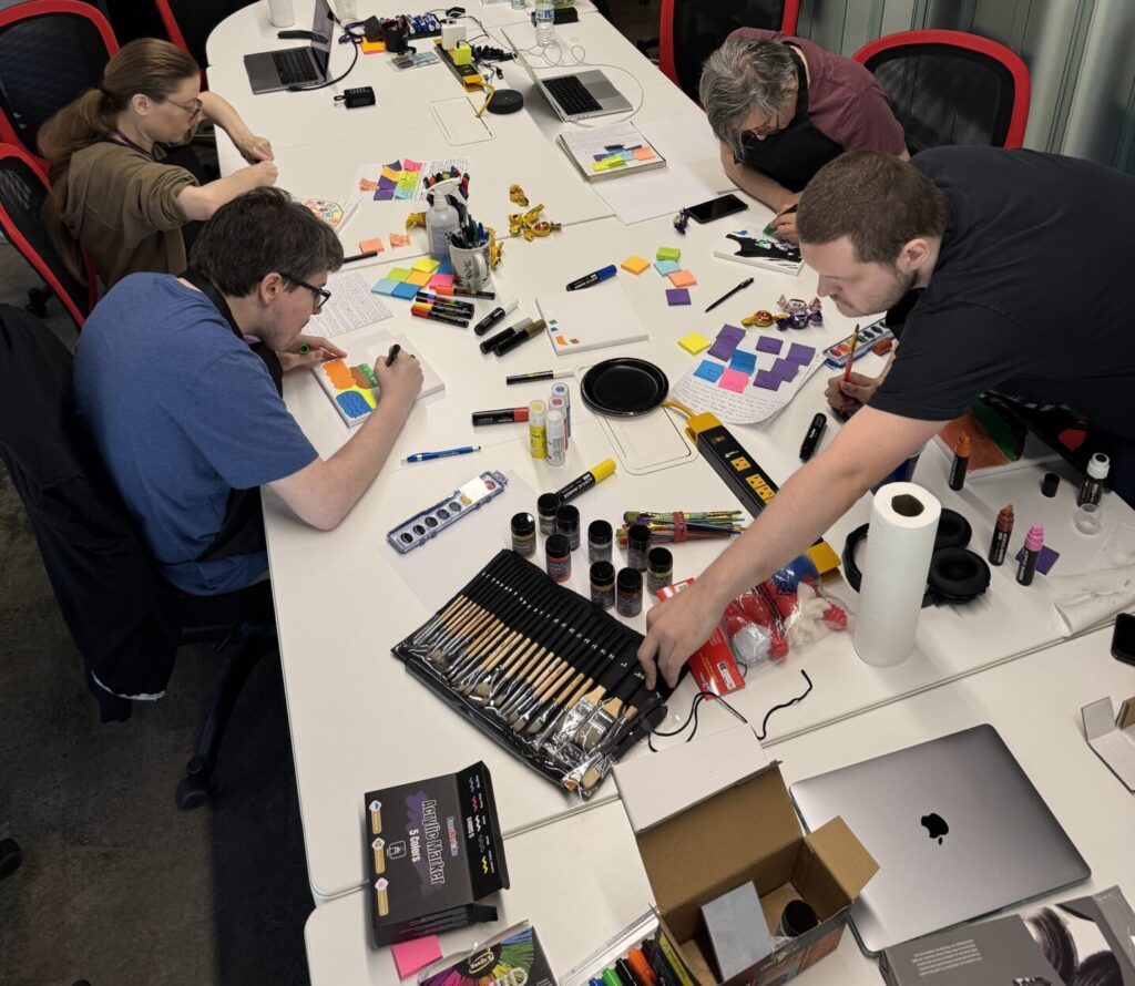 A small group of Aspiritech team members work at a long conference table covered with art supplies.