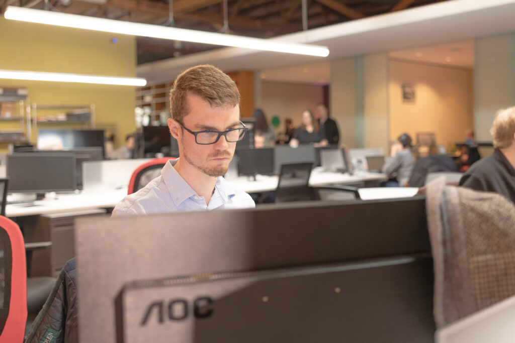 A male Aspiritech employee looks intently at a computer monitor.