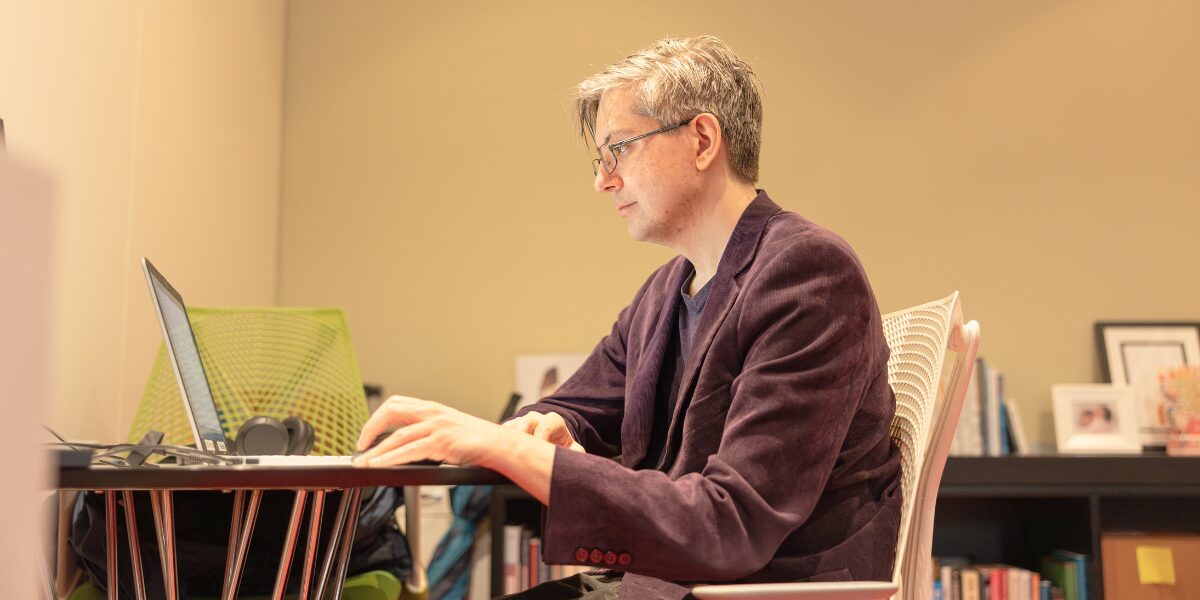 A male Aspiritech employee wearing a burgundy suit coat works at a laptop.