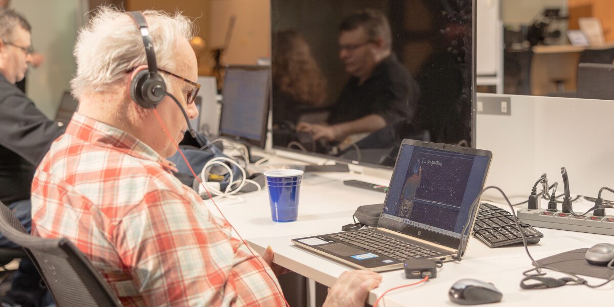 A male Aspiritech employee wearing headphones works at a laptop.