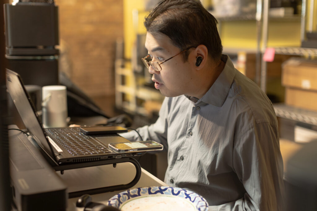A male Aspiritech employee wearing earbuds looks at a laptop screen.