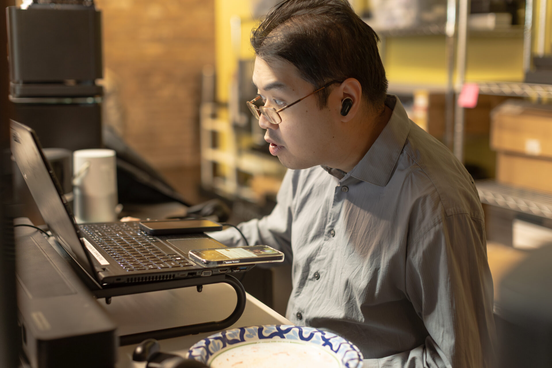 A male Aspiritech employee wearing earbuds looks at a laptop screen.