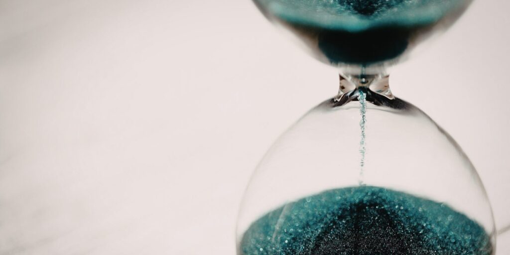 A closeup of an hourglass with teal sand falling from the top to the bottom section.