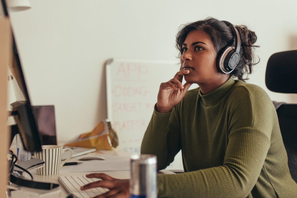 A woman wearing headphones looks at a computer screen.