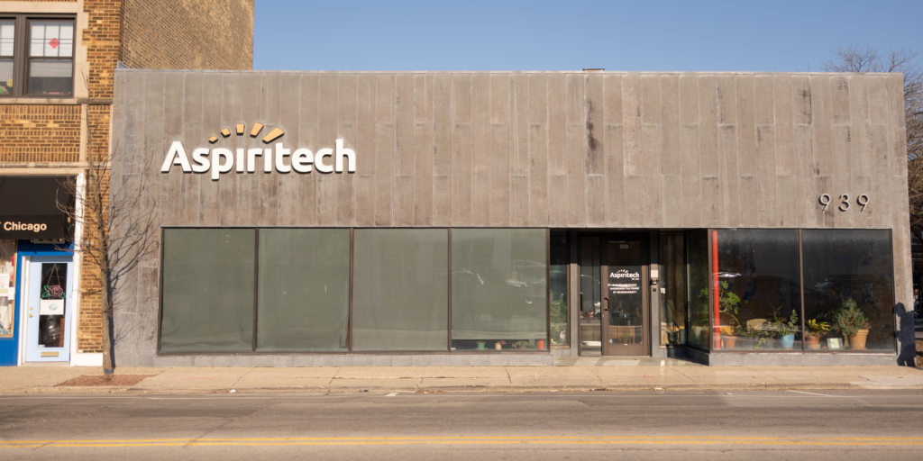 A view of the exterior of Aspiritech's headquarters. It is a single-story concrete building with large glass windows on one side.