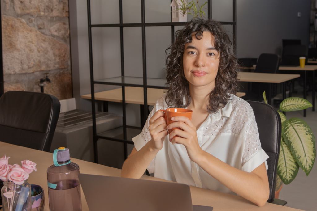 A person holds a mug while sitting at their laptop.