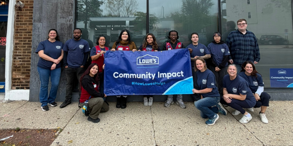 A group photo of Lowe's Red Vest Day volunteers and Aspiritech team members holding a banner reading "Lowe's Community Impact #HowLowesHelps."
